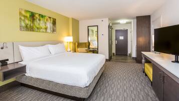 A hotel room with a large bed, bedside table, lamp, and a TV.