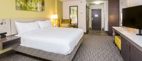 A hotel room with a large bed, bedside table, lamp, and a TV.