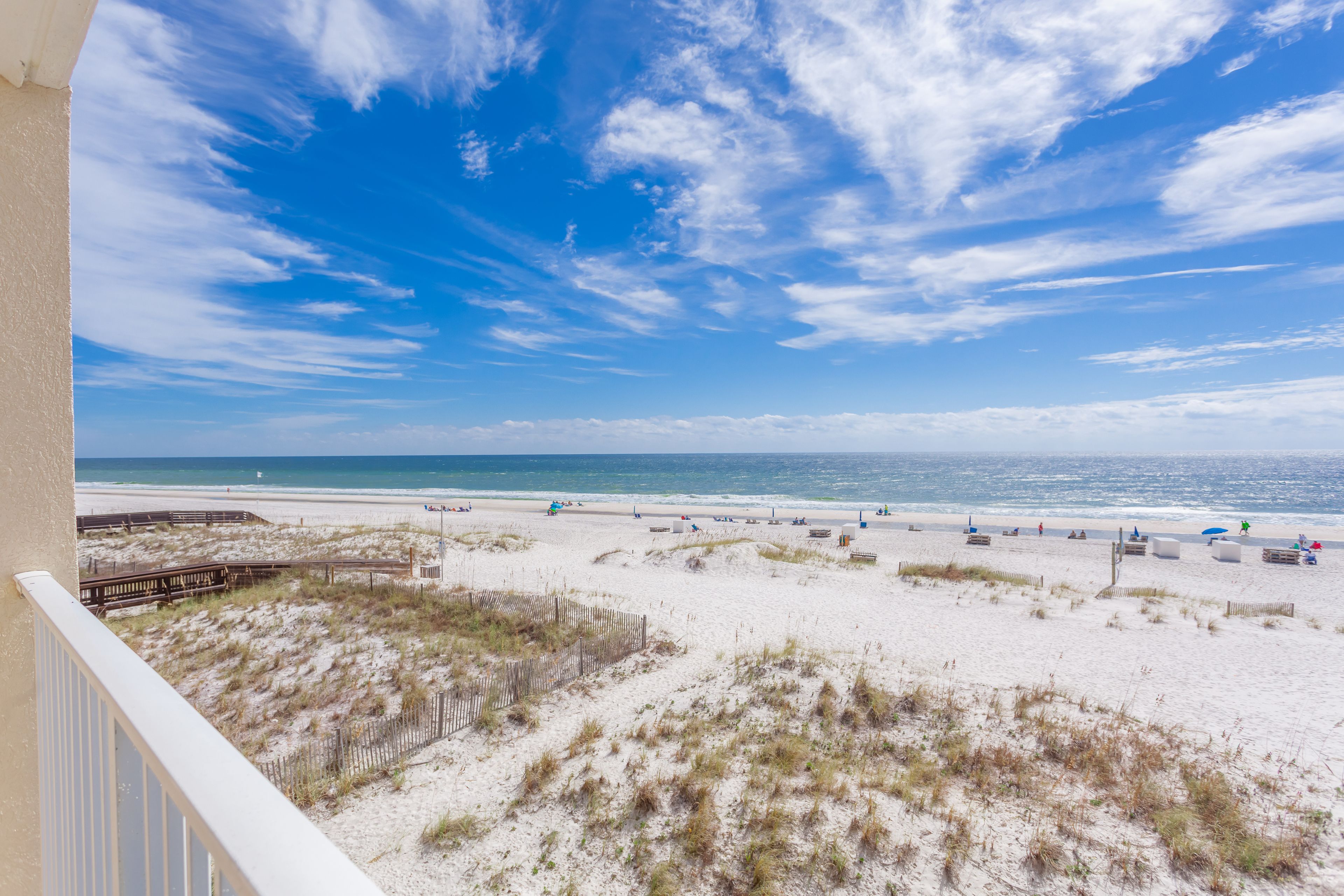 A beach view from a balcony with a wooden deck, sandy beach, and ocean.