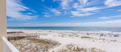 A beach view from a balcony with a wooden deck, sandy beach, and ocean.