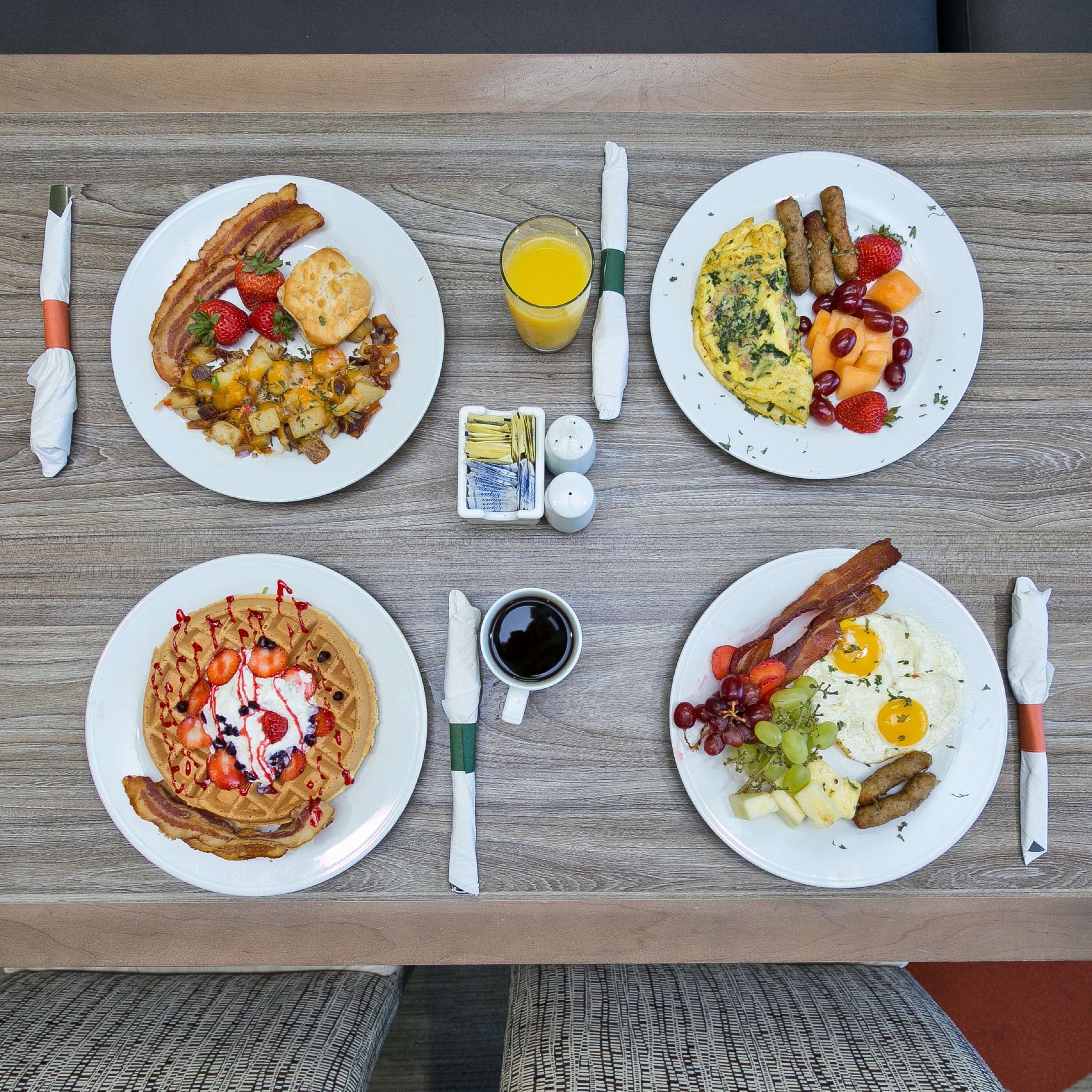 Ett frukostbord med fyra tallrikar mat, ett glas apelsinjuice och olika tillbehör.