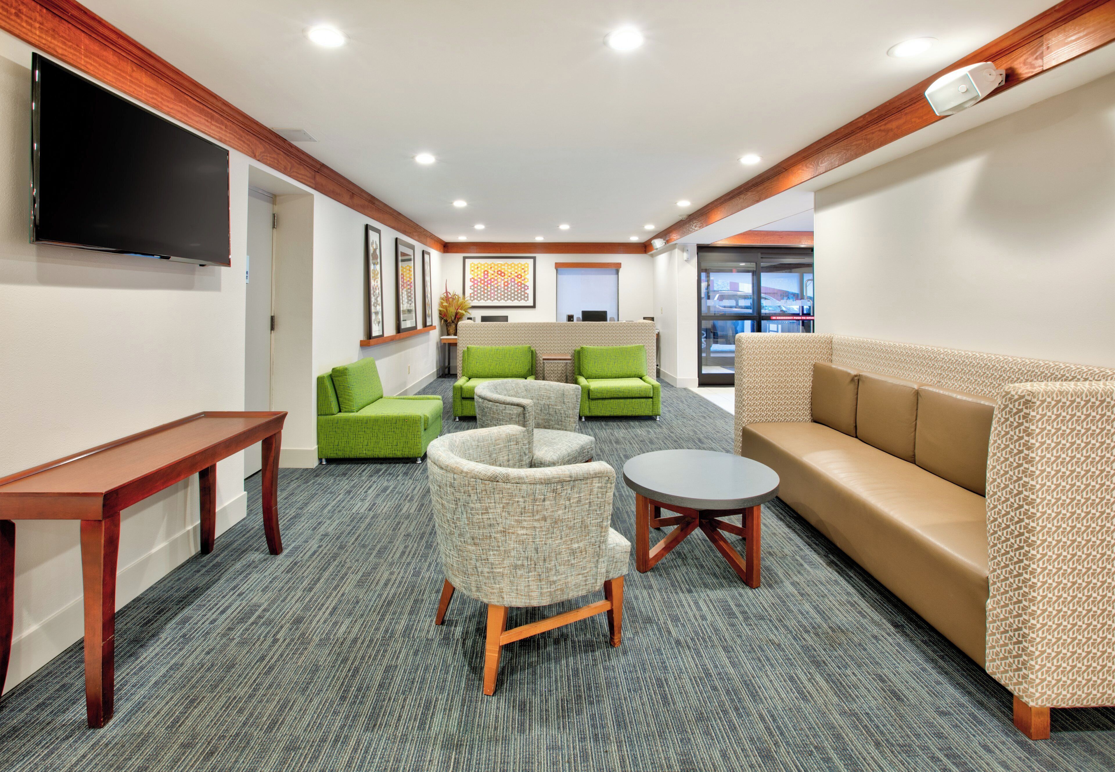 A modern lounge area with a flat-screen TV, green and beige seating, a small round table, and a patterned sofa.