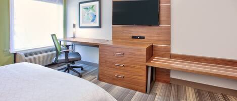 Habitación de hotel con cama, escritorio con silla, televisor de pantalla plana montado en una pared de madera y un ventanal grande.