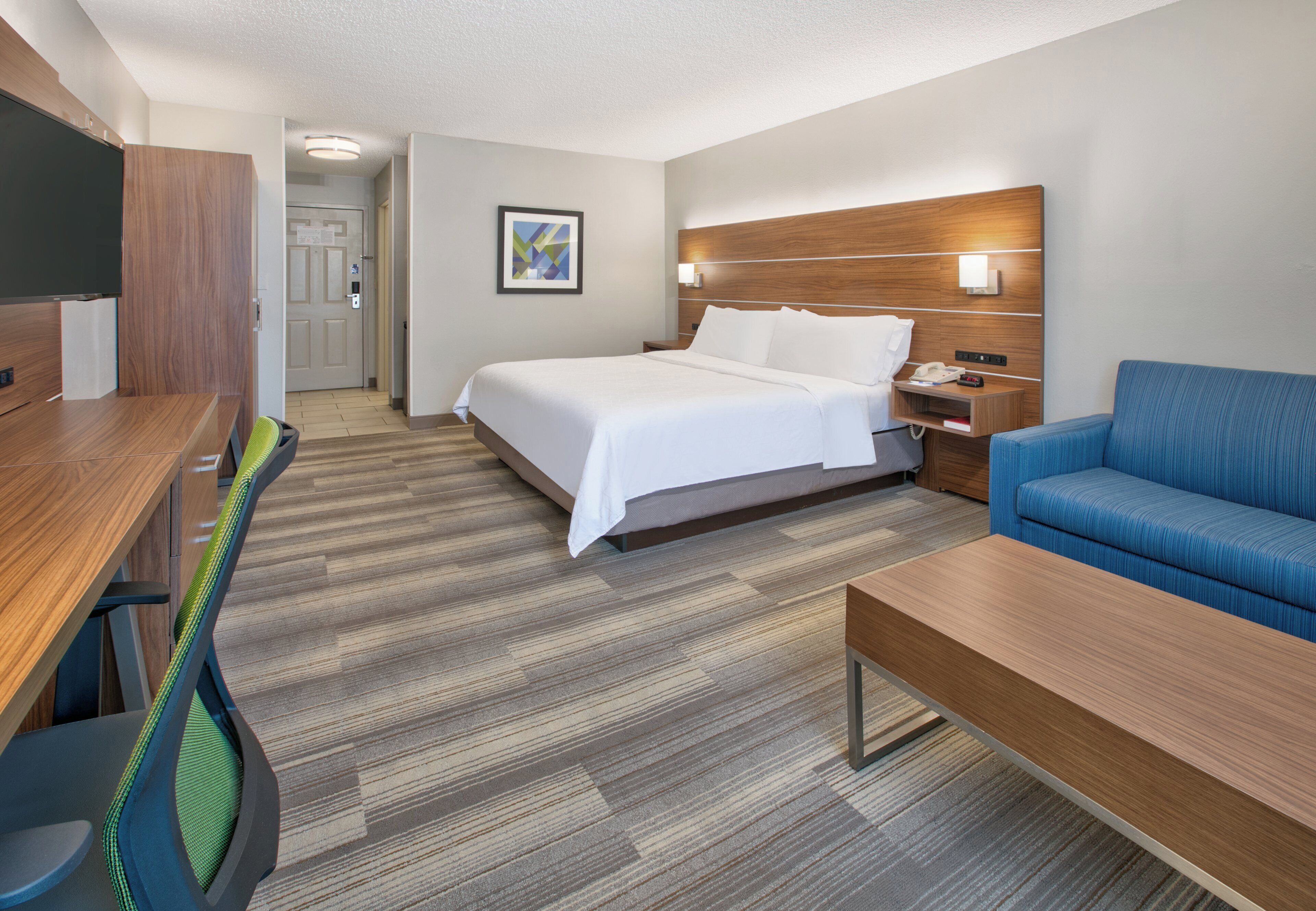 Una habitación de hotel con cama, escritorio, silla, sofá y mesita de noche.