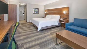 Una habitación de hotel con cama, escritorio, silla, sofá y mesita de noche.