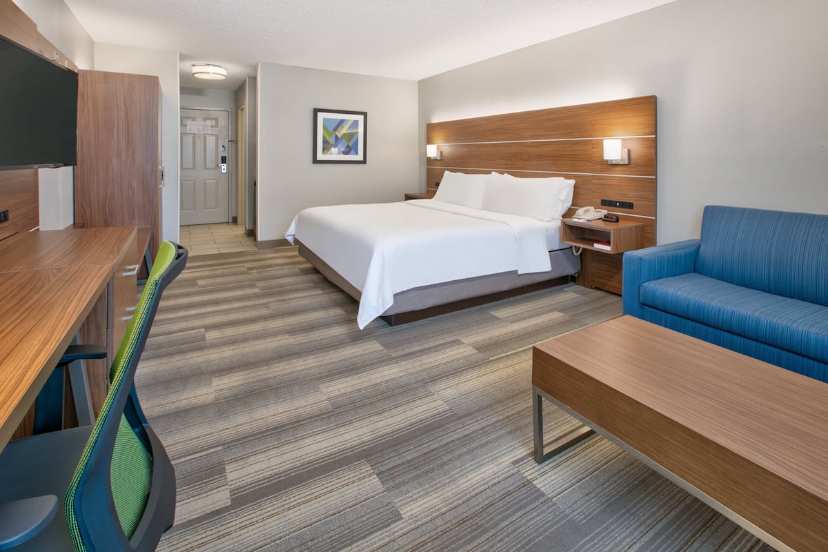 A hotel room with a bed, a desk, a chair, a sofa, and a nightstand.