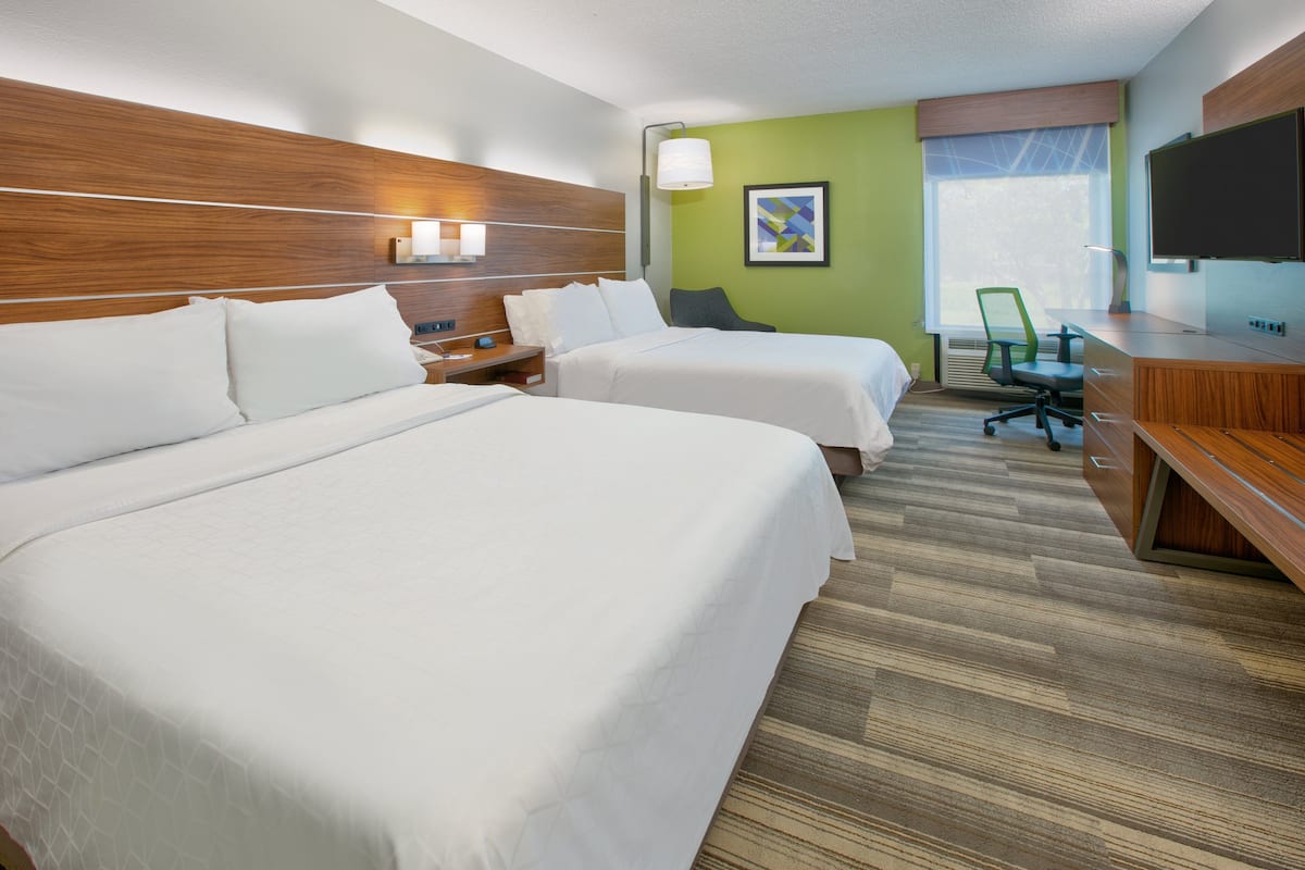 A hotel room with two beds, a desk with a computer, a chair, and a TV.