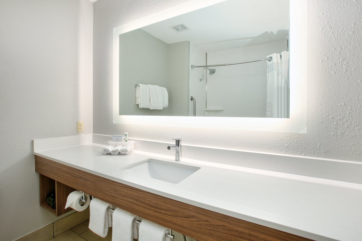A modern bathroom with a large mirror, white sink, and wooden vanity.