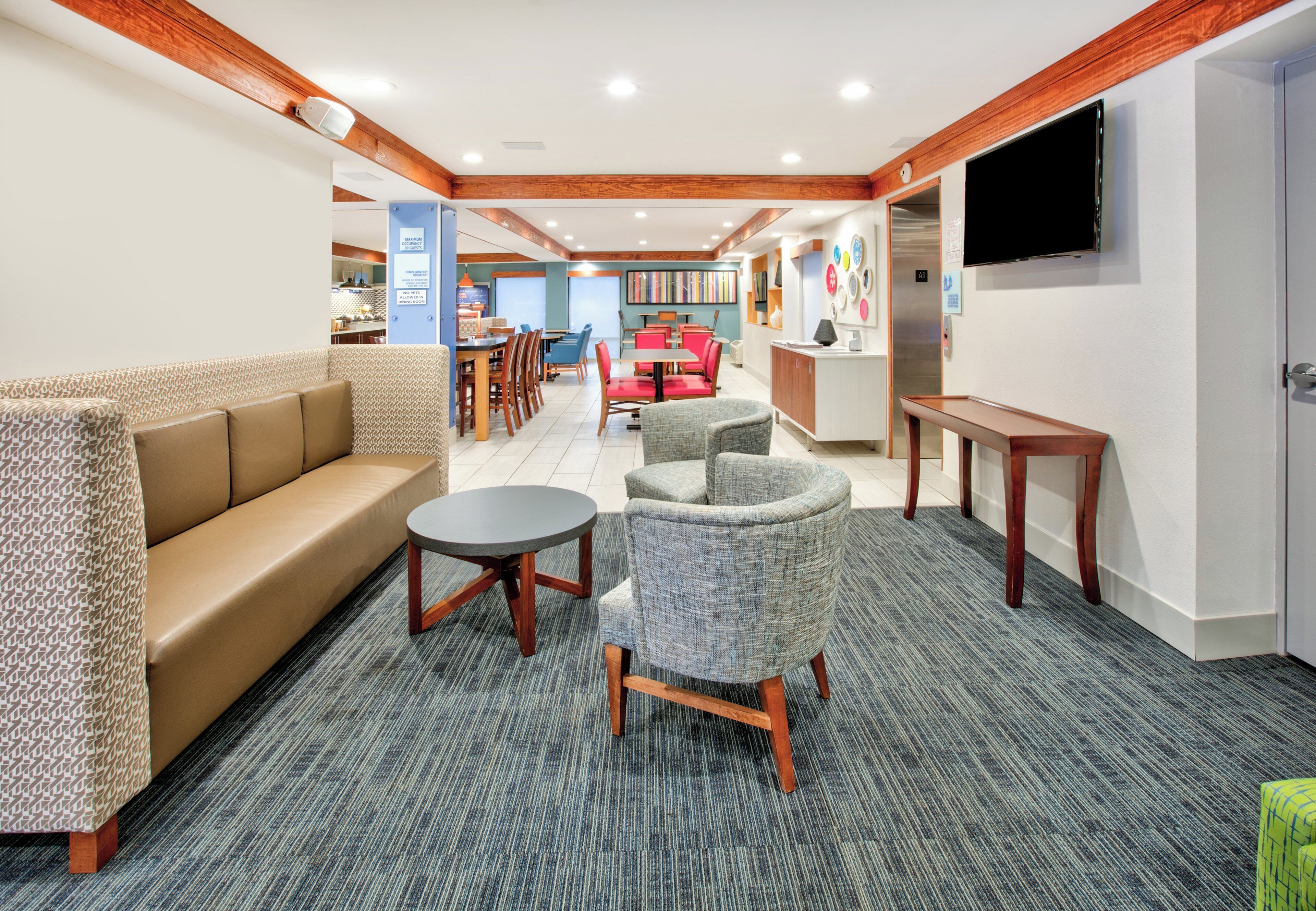 A hotel lobby with a sofa, armchairs, a small table, and a television on the wall.