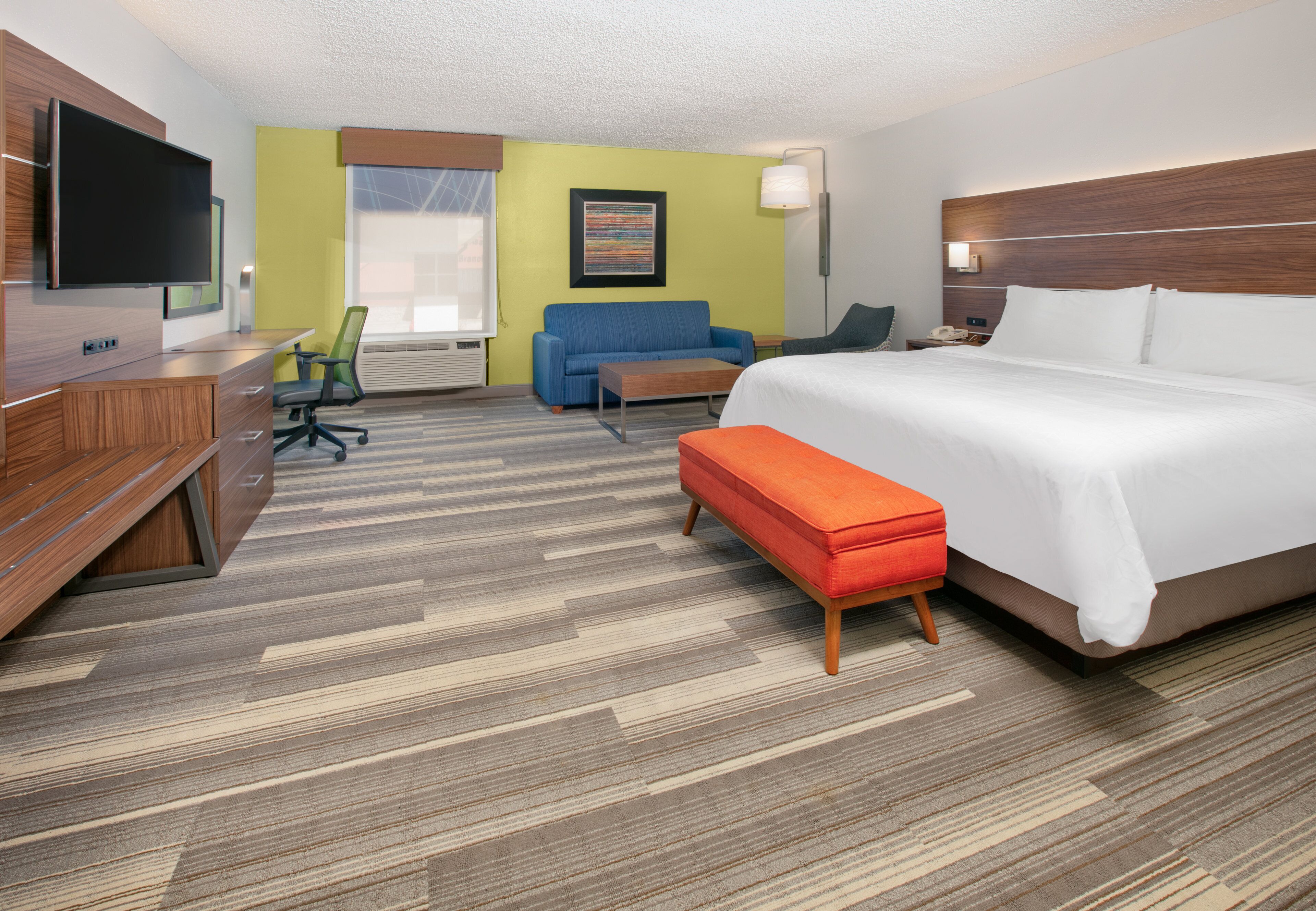 A hotel room with a bed, a desk, a chair, a sofa, and a TV.