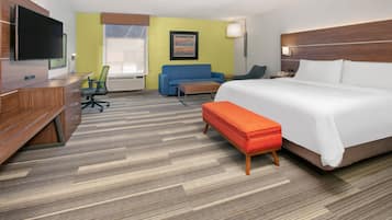 A hotel room with a bed, a desk, a chair, a sofa, and a TV.