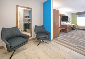 A hotel room with two grey armchairs, a desk with a flat-screen TV, a microwave, and a mini-fridge.