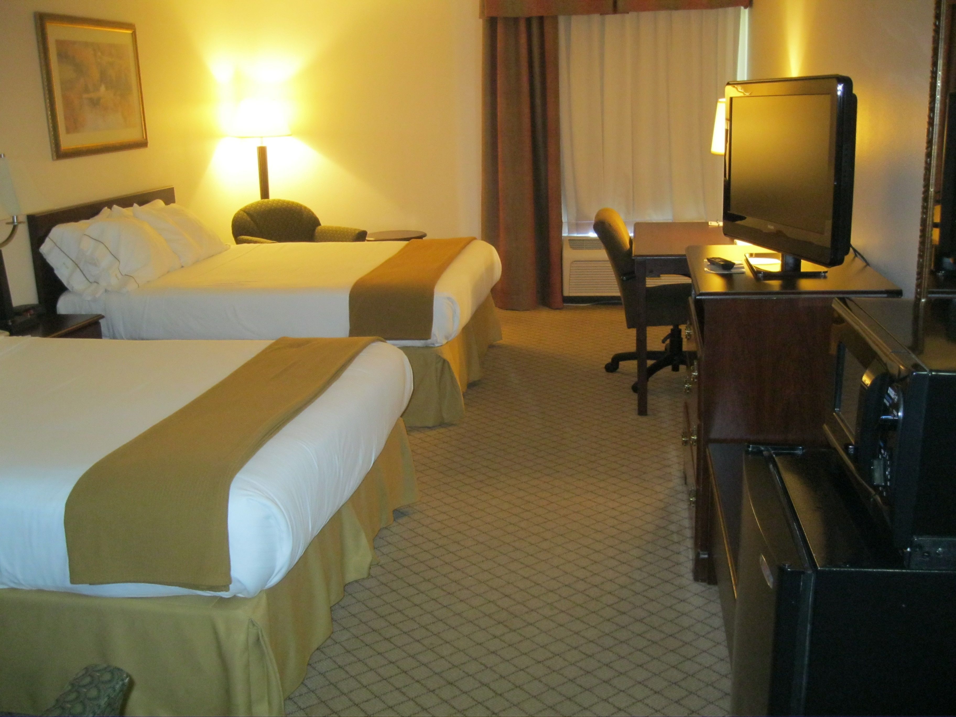 A hotel room with two beds, a desk with a computer, a TV, and a chair.