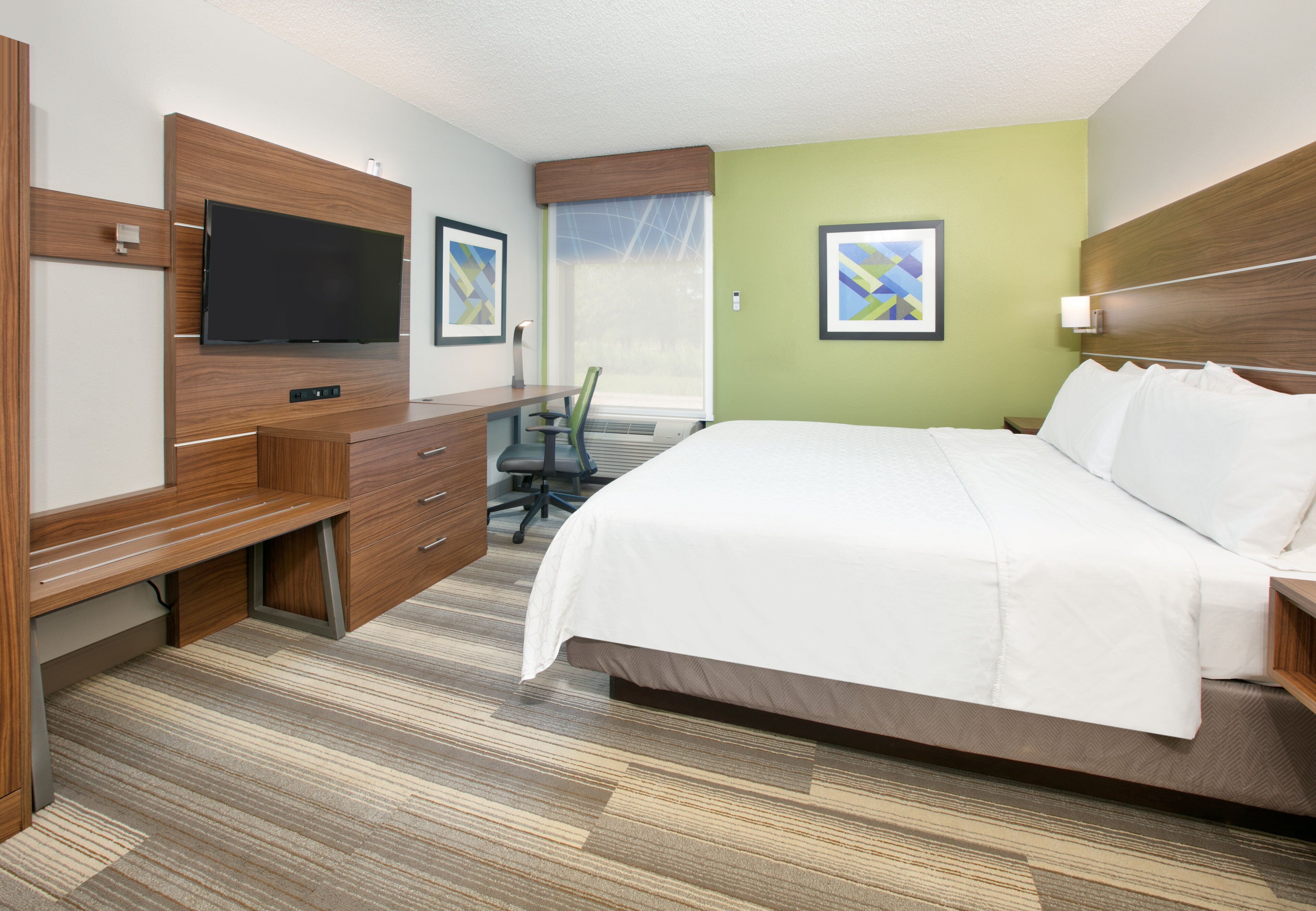 A hotel room with a large bed, a desk with a chair, a flat-screen TV, and artwork on the walls.