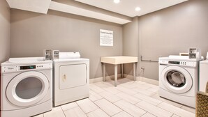 A laundry area with two front-loading washers, a table, and a sign indicating guest laundry services. - Holiday Inn Express Hope by IHG (Hope)