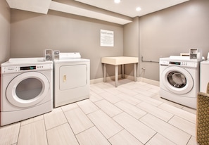 A laundry area with two front-loading washers, a table, and a sign indicating guest laundry services.