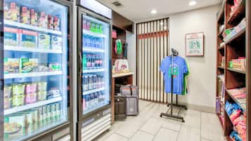 A hotel room with a minibar, a refrigerator stocked with beverages, a suitcase, and a t-shirt on a rack.