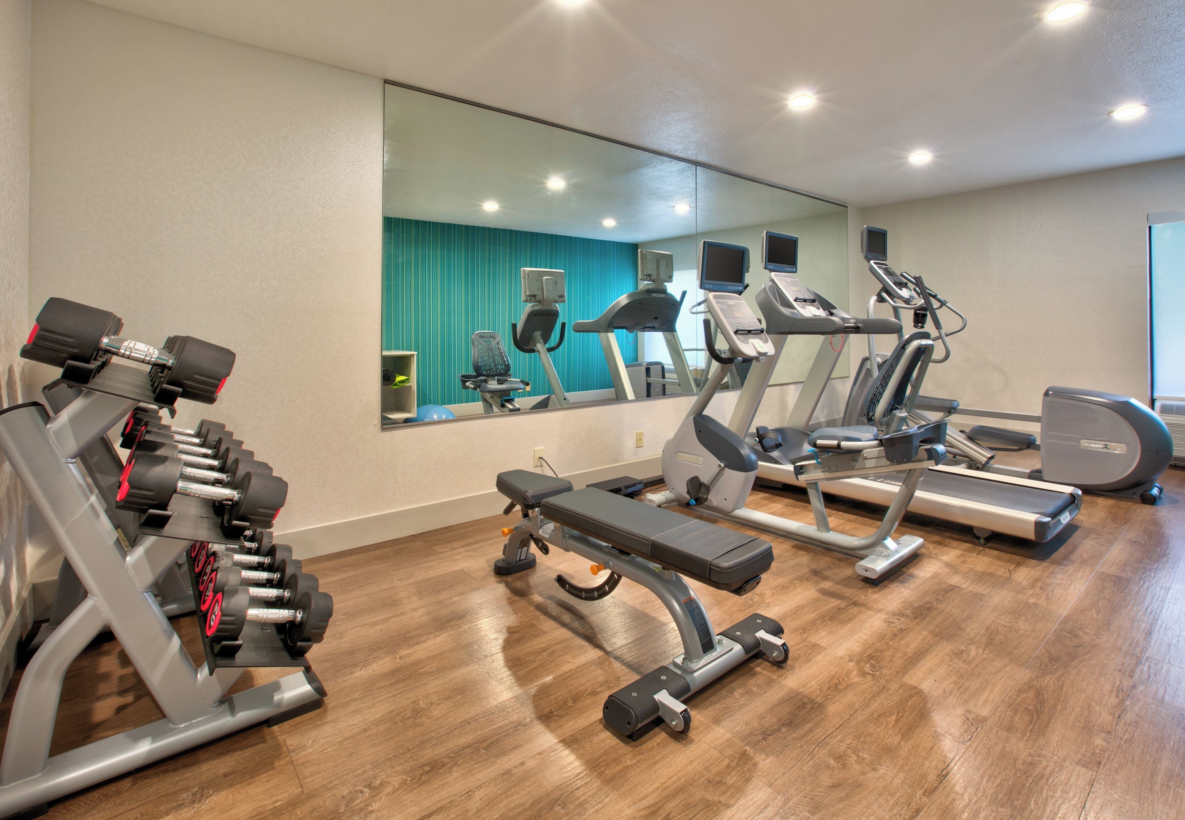 Un gimnasio con equipo de ejercicio variado, incluyendo cintas de correr, una prensa de banca y mancuernas.