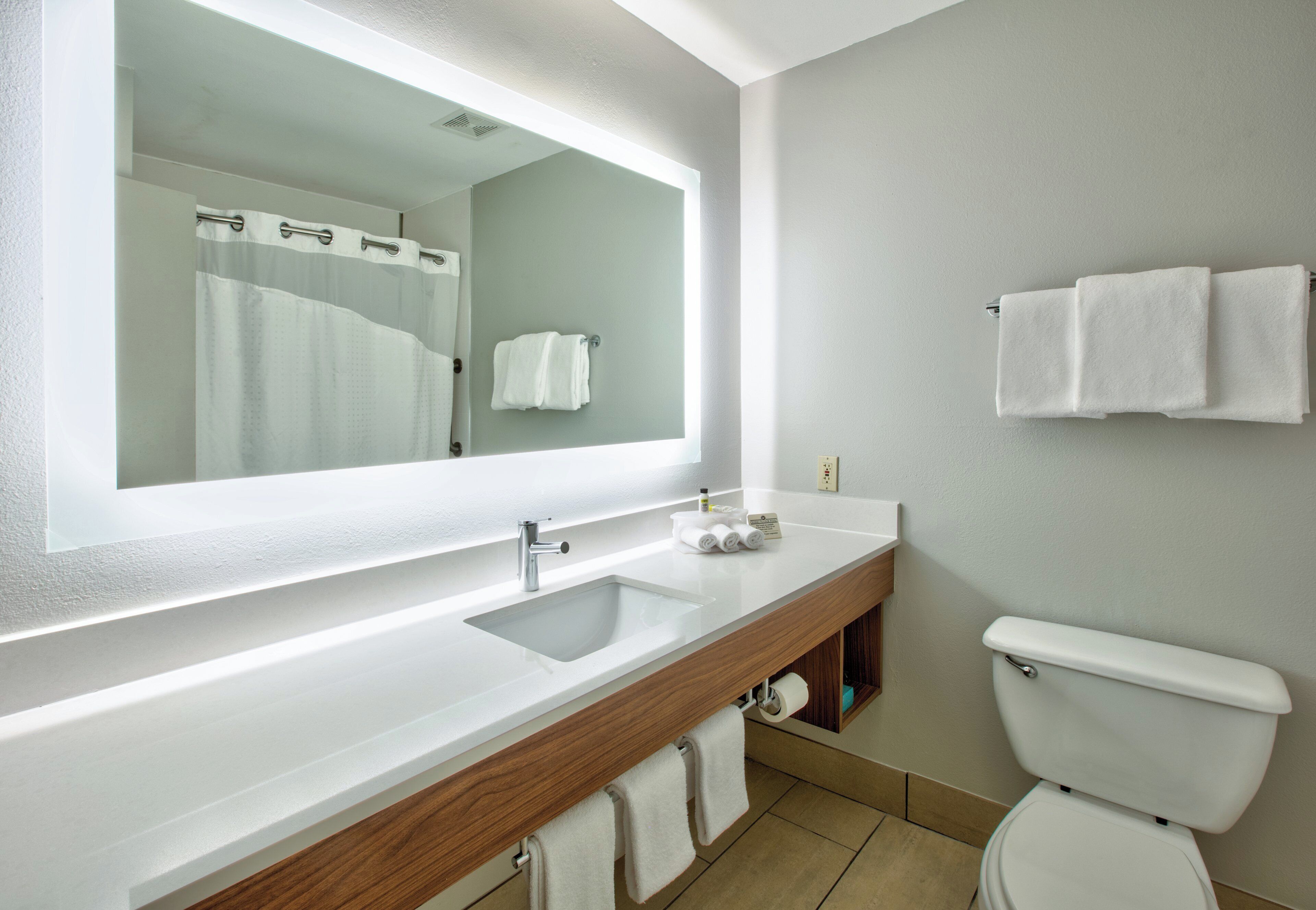 Un baño moderno con un espejo grande, un lavabo, un inodoro y un perchero para toallas.