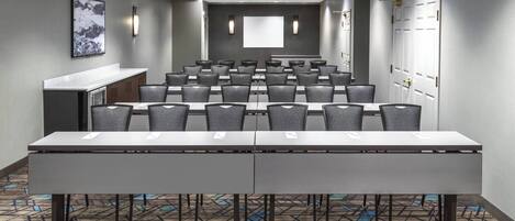 A conference room with a long table, rows of chairs, a projector screen, and a whiteboard.