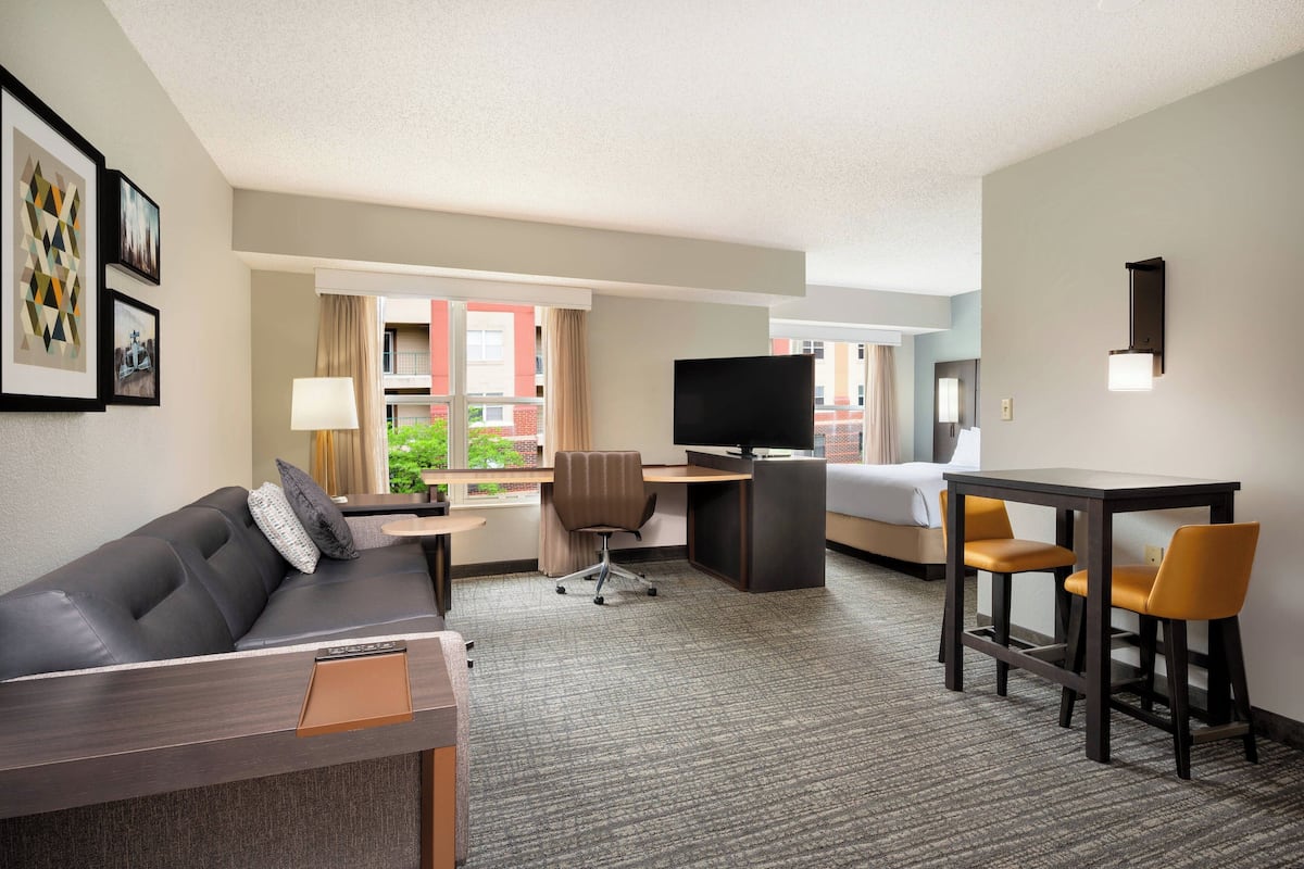 A hotel room with a sofa, a desk with a TV, a bed, and a dining area.