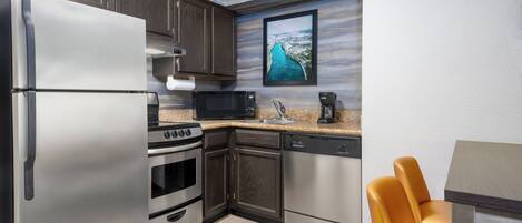 A compact kitchen with a refrigerator, microwave, stove, oven, and dishwasher. There's a framed picture on the wall and a dining area with a table and chairs.