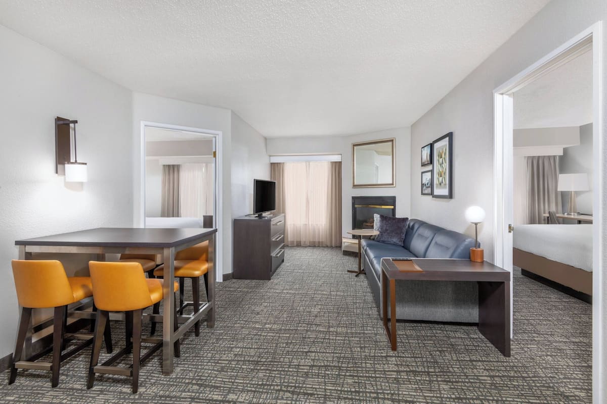A hotel room with a dining area, a sofa, a TV, and a lamp.