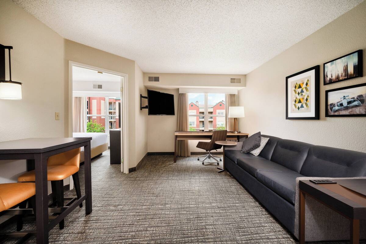 A hotel room with a desk, sofa, and a view of buildings outside.