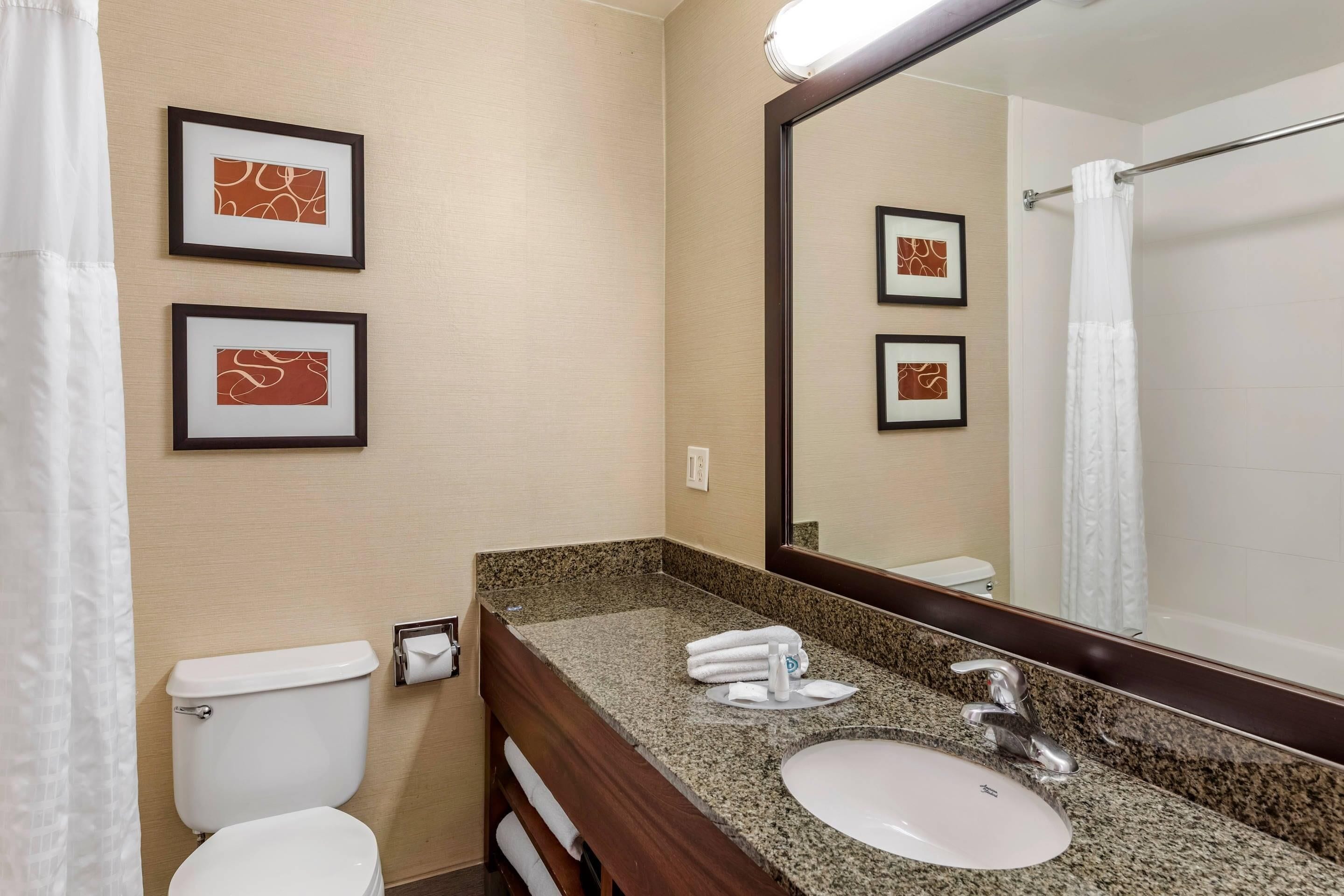 A bathroom with a toilet, sink, and mirror. There are framed pictures on the wall.
