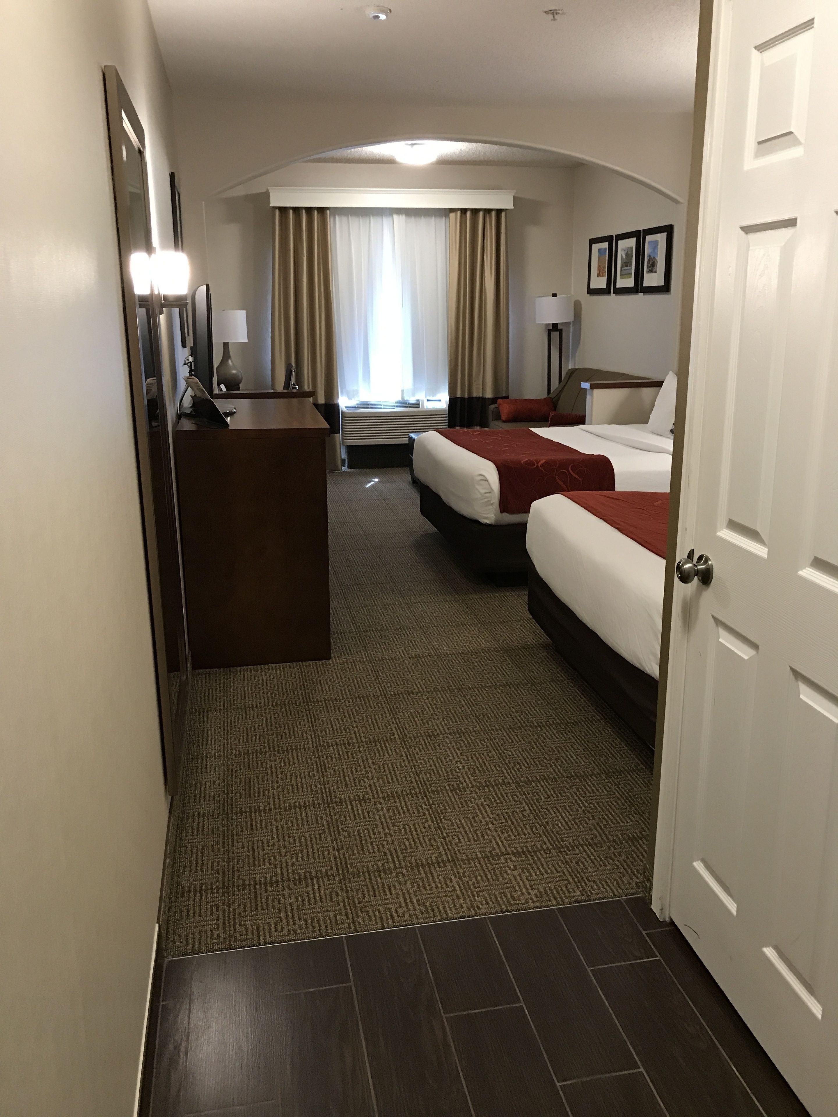 A hotel room with two beds, a desk, a chair, a lamp, and a window with curtains.