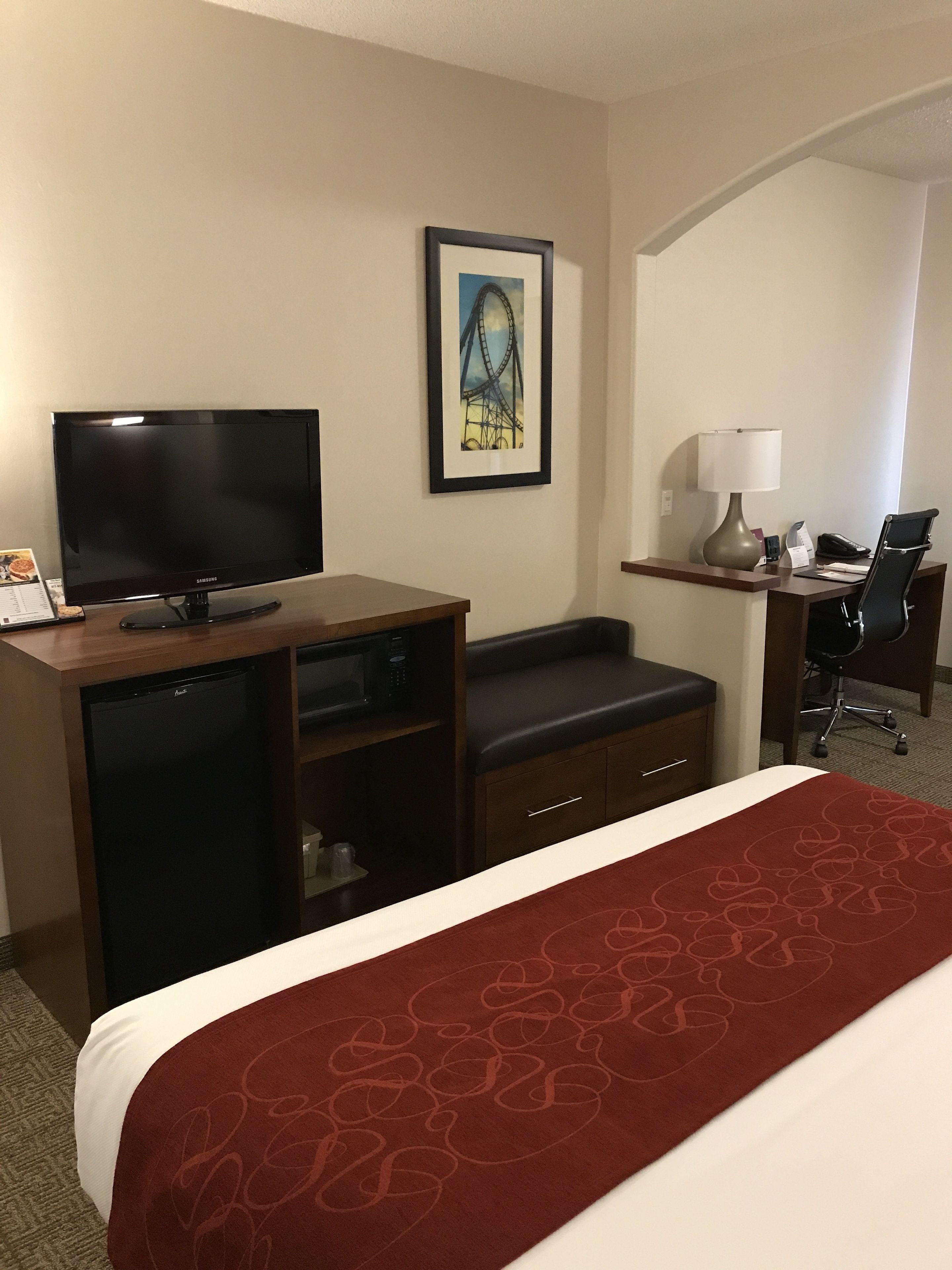 Ein Hotelzimmer mit Bett, Schreibtisch mit Computer, Fernseher, Mikrowelle und Kühlschrank.
