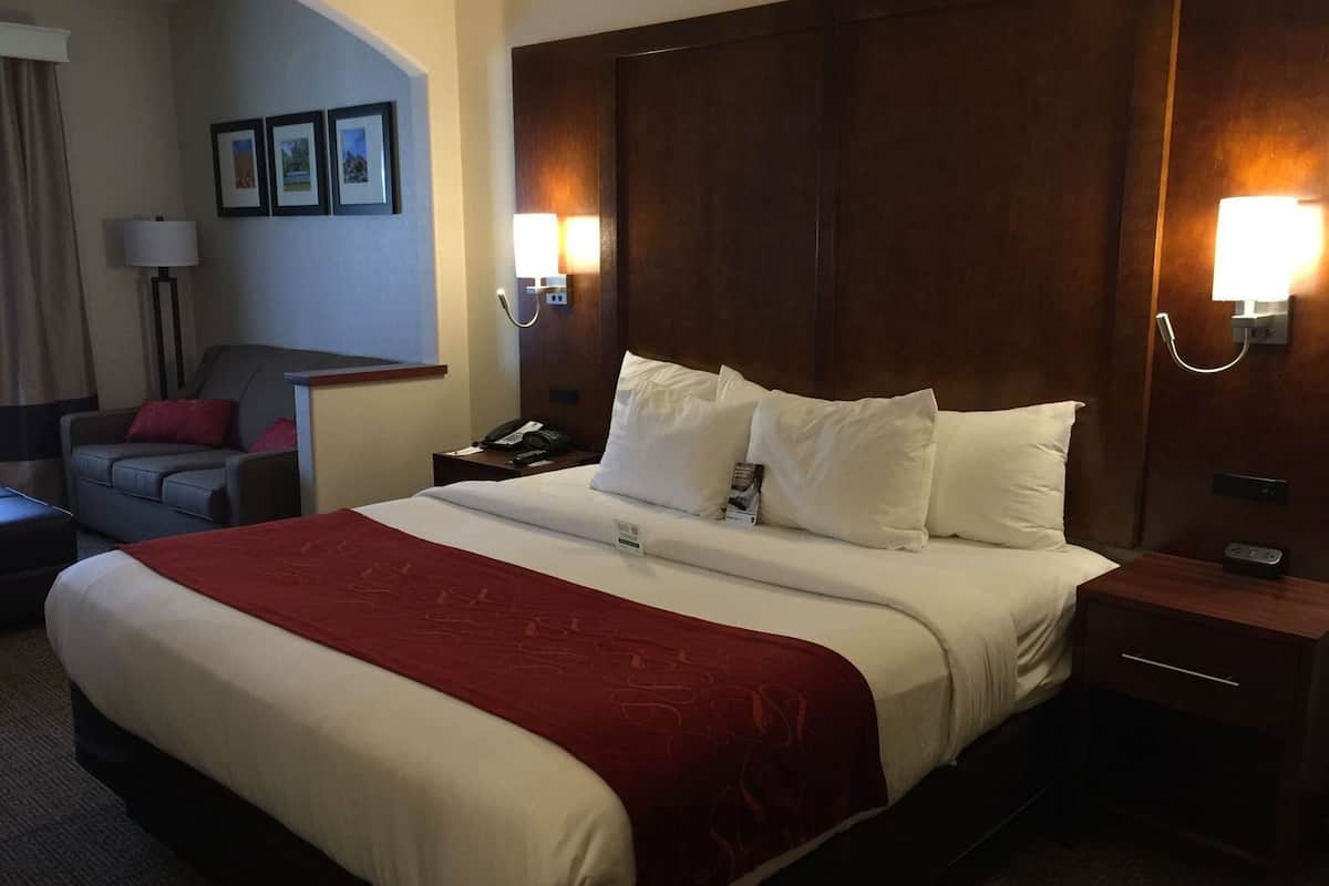 A hotel room with a large bed, a desk, a chair, and a lamp.