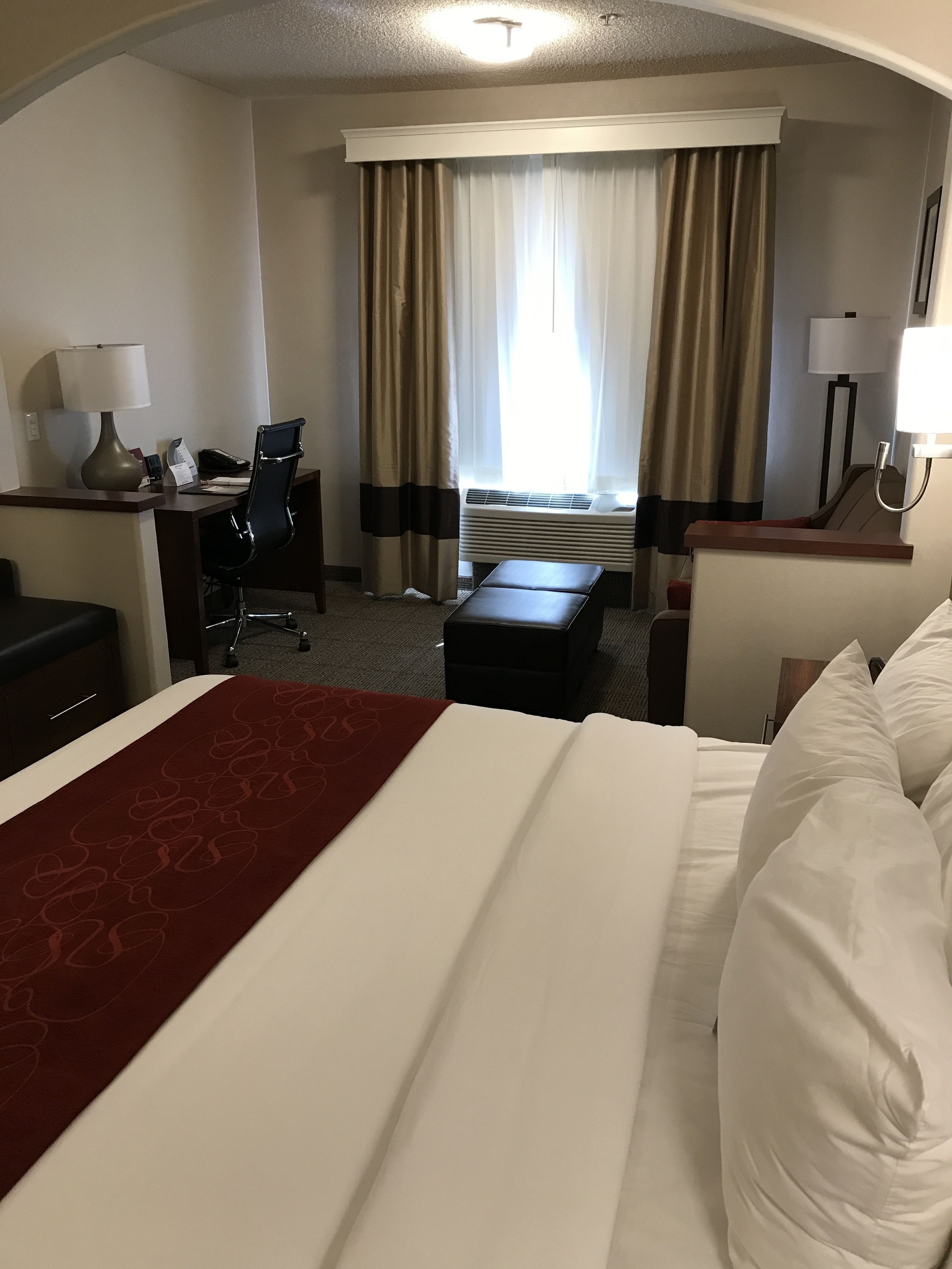 Ett hotellrum med en säng, ett skrivbord, en stol och utsikt över omgivningarna genom stora fönster.