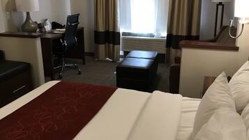 Una camera d'albergo con un letto, una scrivania, una sedia e vista sull'esterno attraverso ampie finestre.