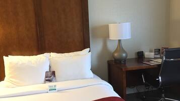 Habitación de hotel con cama, escritorio, silla, lámpara y un cartel en el escritorio.