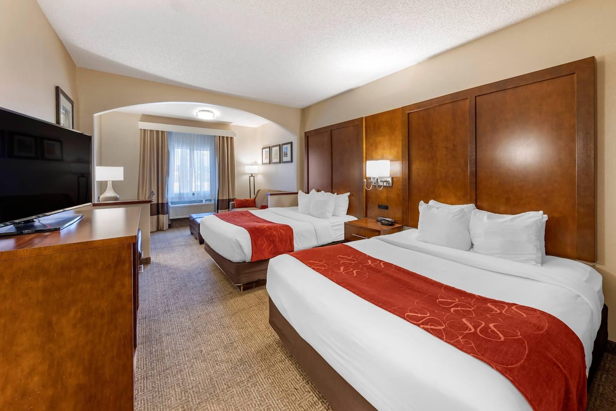 A hotel room with two beds, a desk, a TV, and a bathroom visible through an archway.