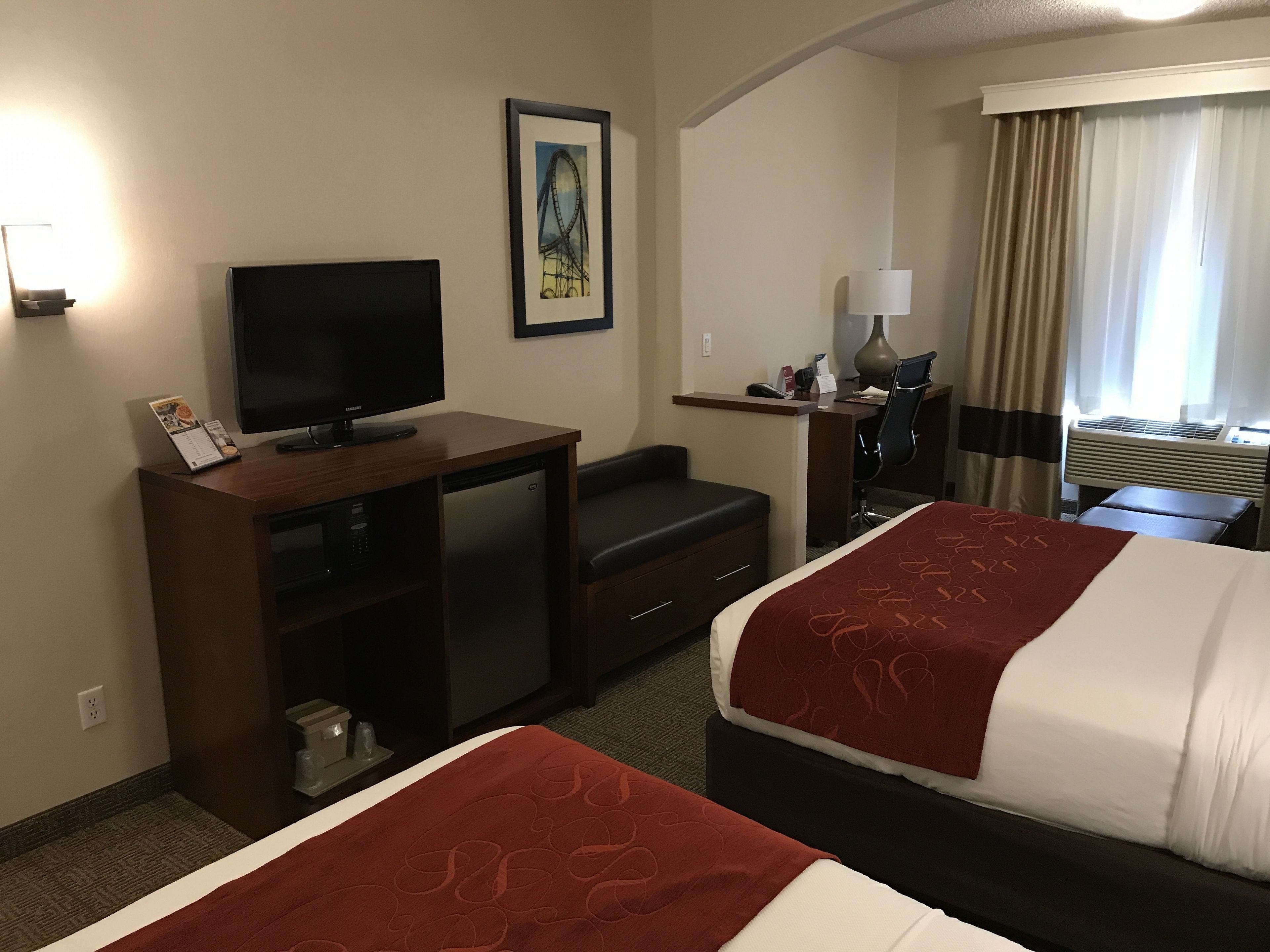 Une chambre d’hôtel avec deux lits, un bureau avec une télévision, une chaise, une lampe de bureau et un tableau encadré au mur.