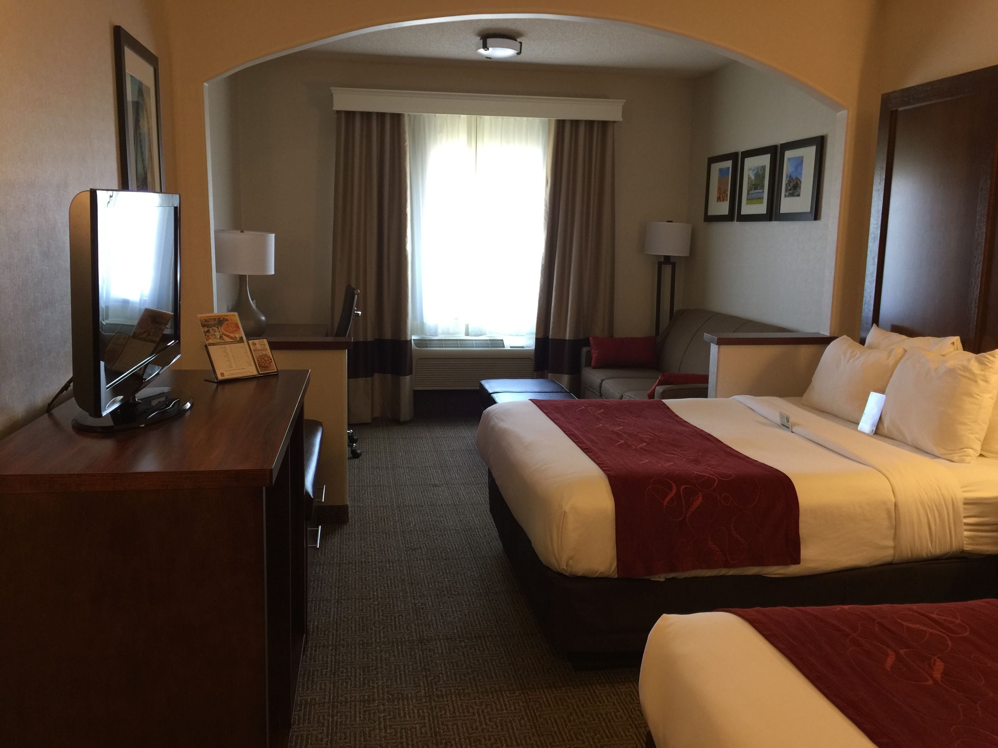 A hotel room with a bed, a desk, a chair, a TV, and a window with curtains.