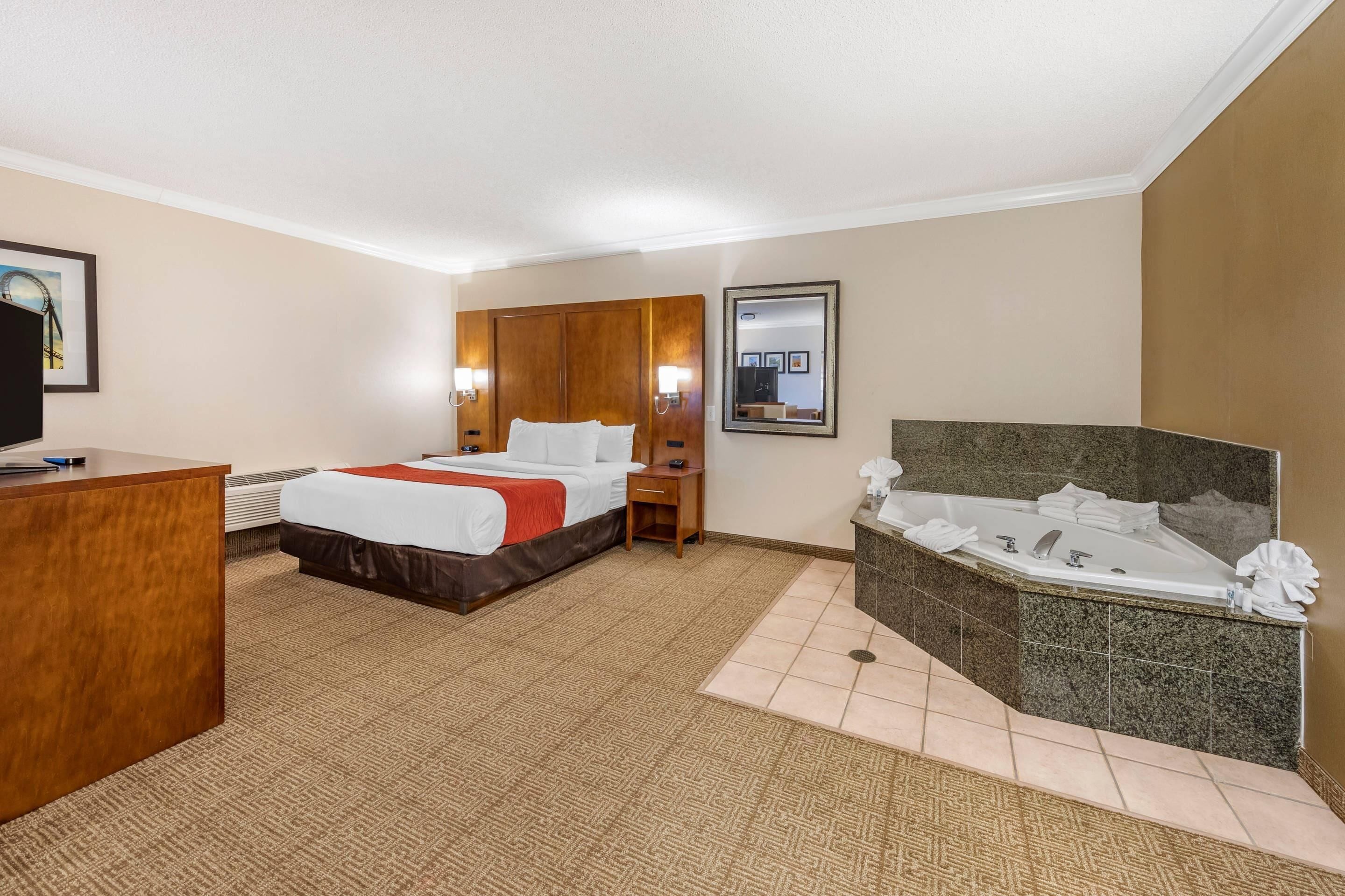 A hotel room with a bed, a desk, a chair, a bathroom with a bathtub, and a mirror.