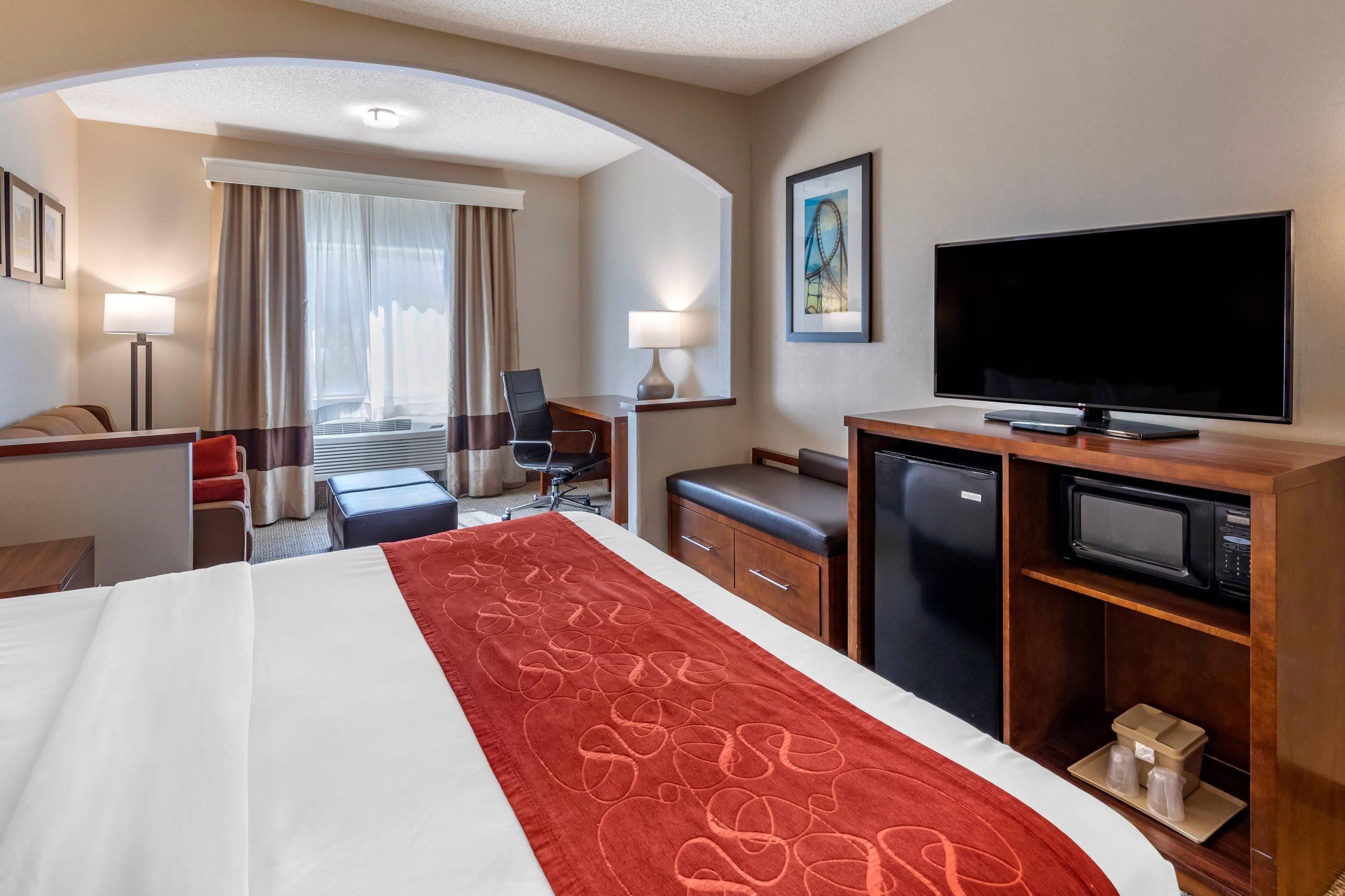 A hotel room with a large bed, a television, a desk with a computer, a refrigerator, and a microwave.