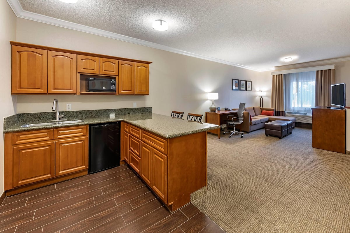 A hotel room with a kitchen area, a dining table, a sofa, and a flat-screen TV.
