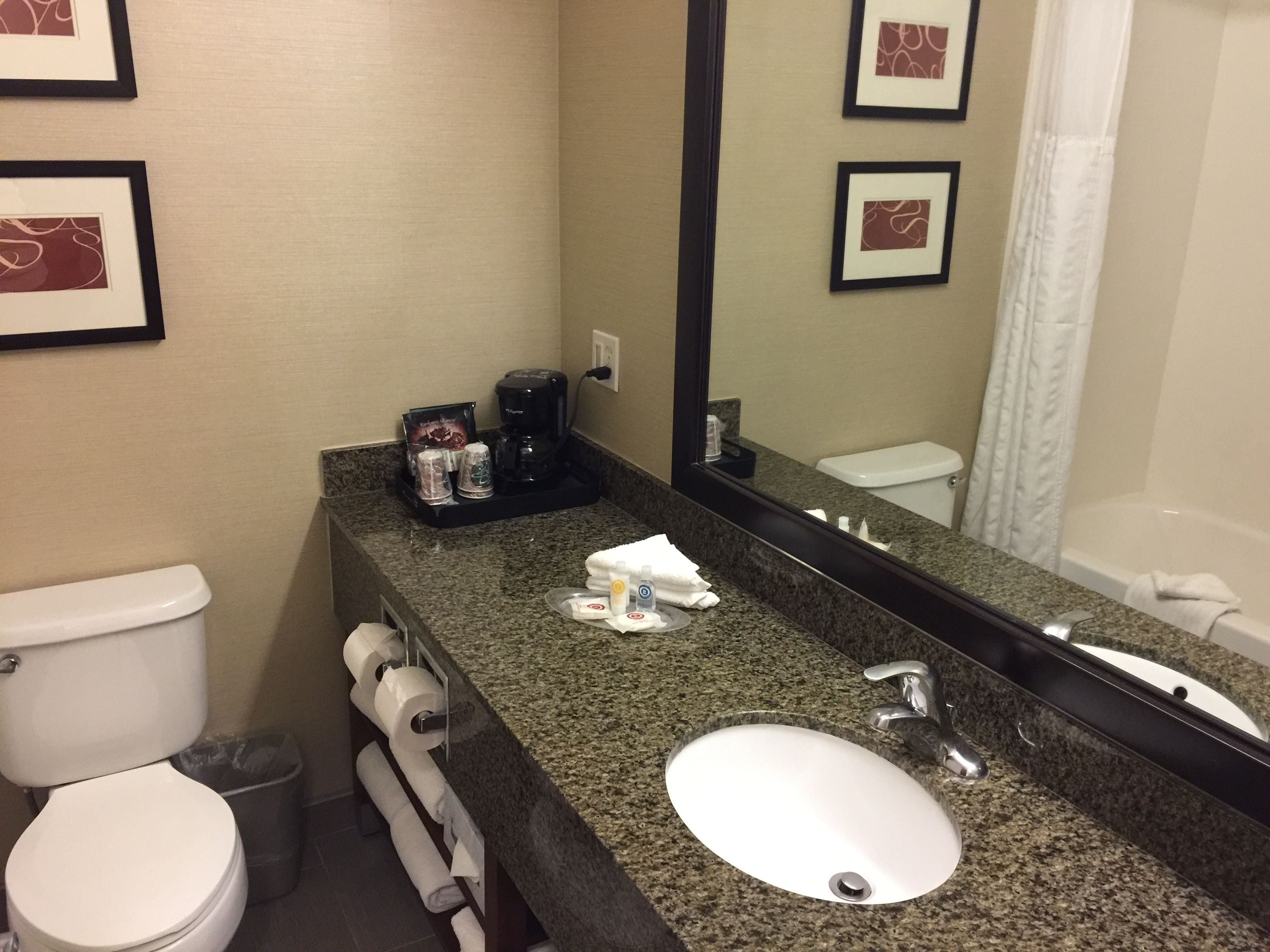 Une salle de bain avec des toilettes blanches, un lavabo avec un miroir et des tableaux encadrés accrochés au mur.