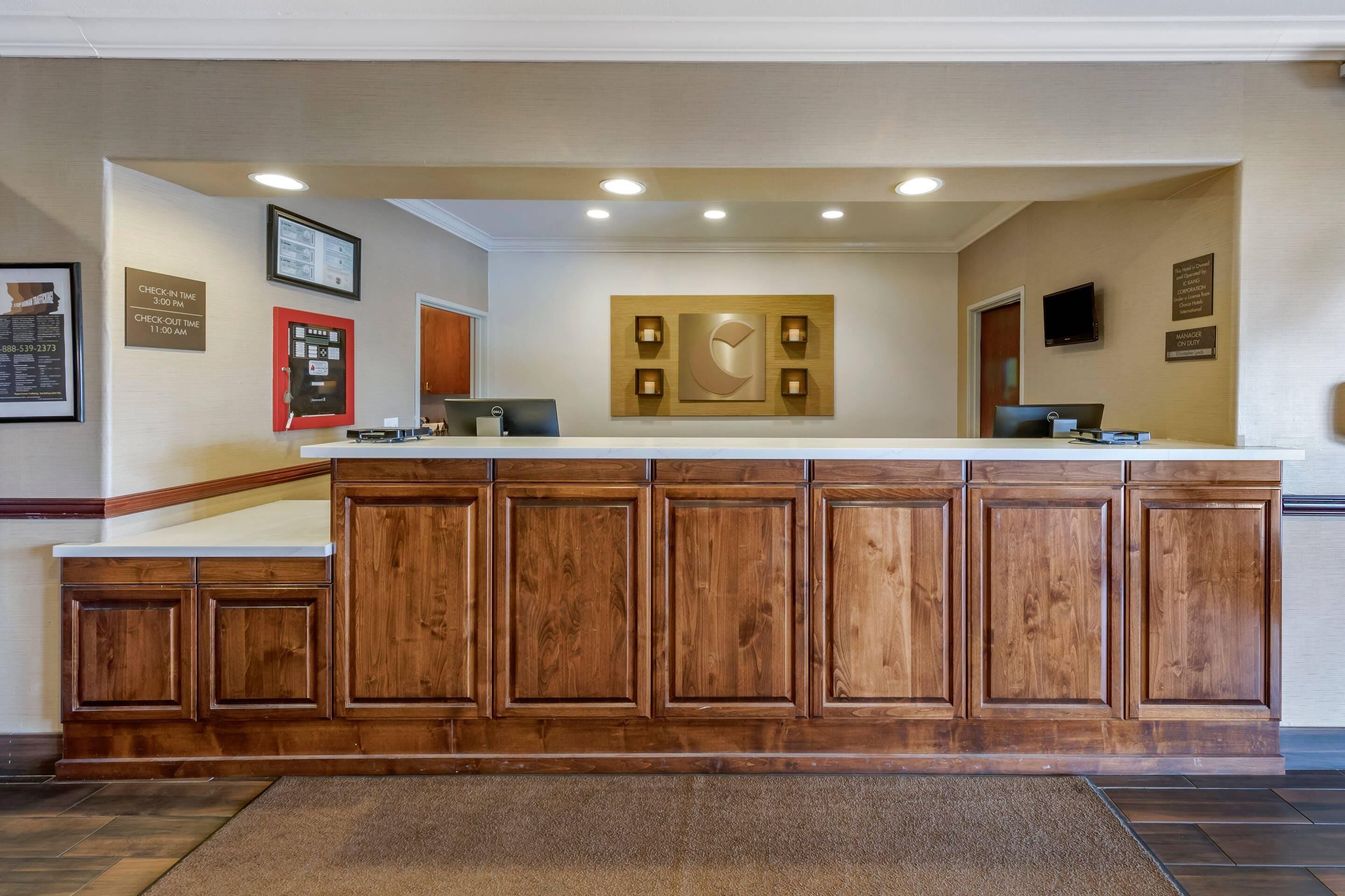 A reception desk with a wooden finish, a check-in/out sign, a digital display, and a mounted artwork.
