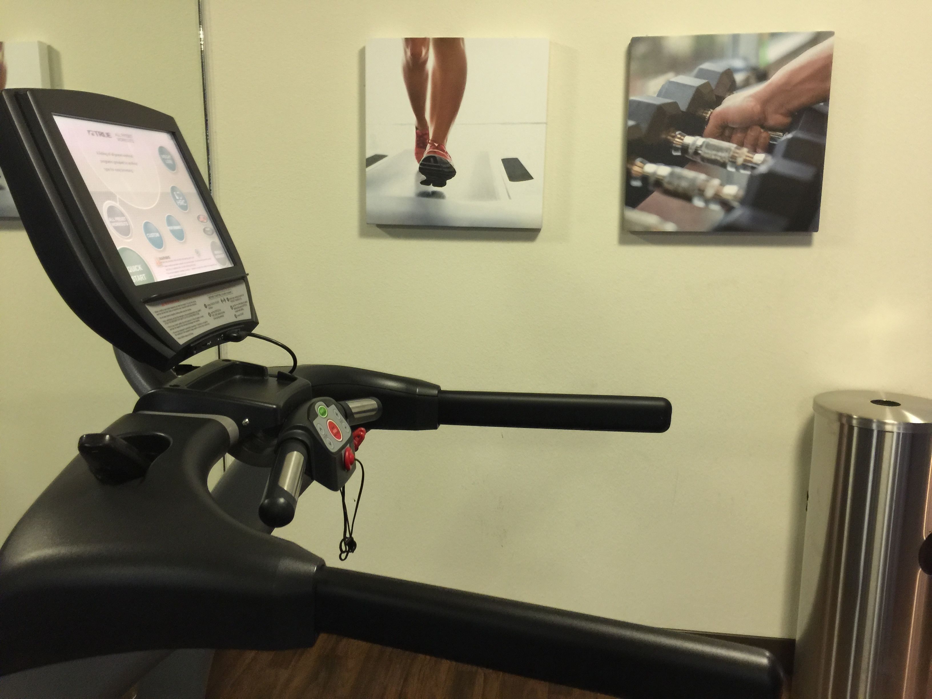A stationary bike with a digital display, a wall-mounted poster of a person running, and a poster of a person lifting weights.