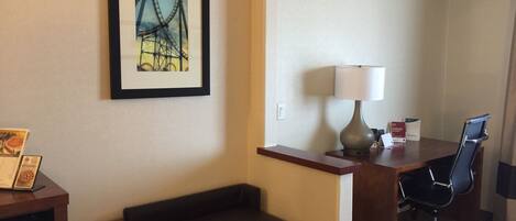 Habitación de hotel con escritorio, silla, lámpara, cuadro enmarcado de una montaña rusa y una pequeña mesa con un menú.