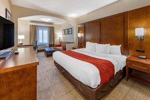 A hotel room with a large bed, a desk, a TV, and a seating area with a chair and a sofa.
