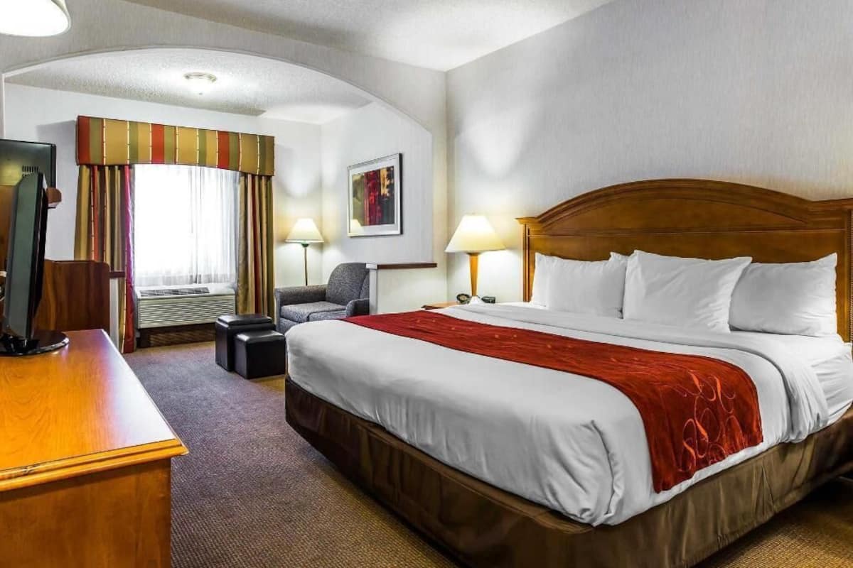 A hotel room with a large bed, a desk, a chair, a TV, and a window with curtains.