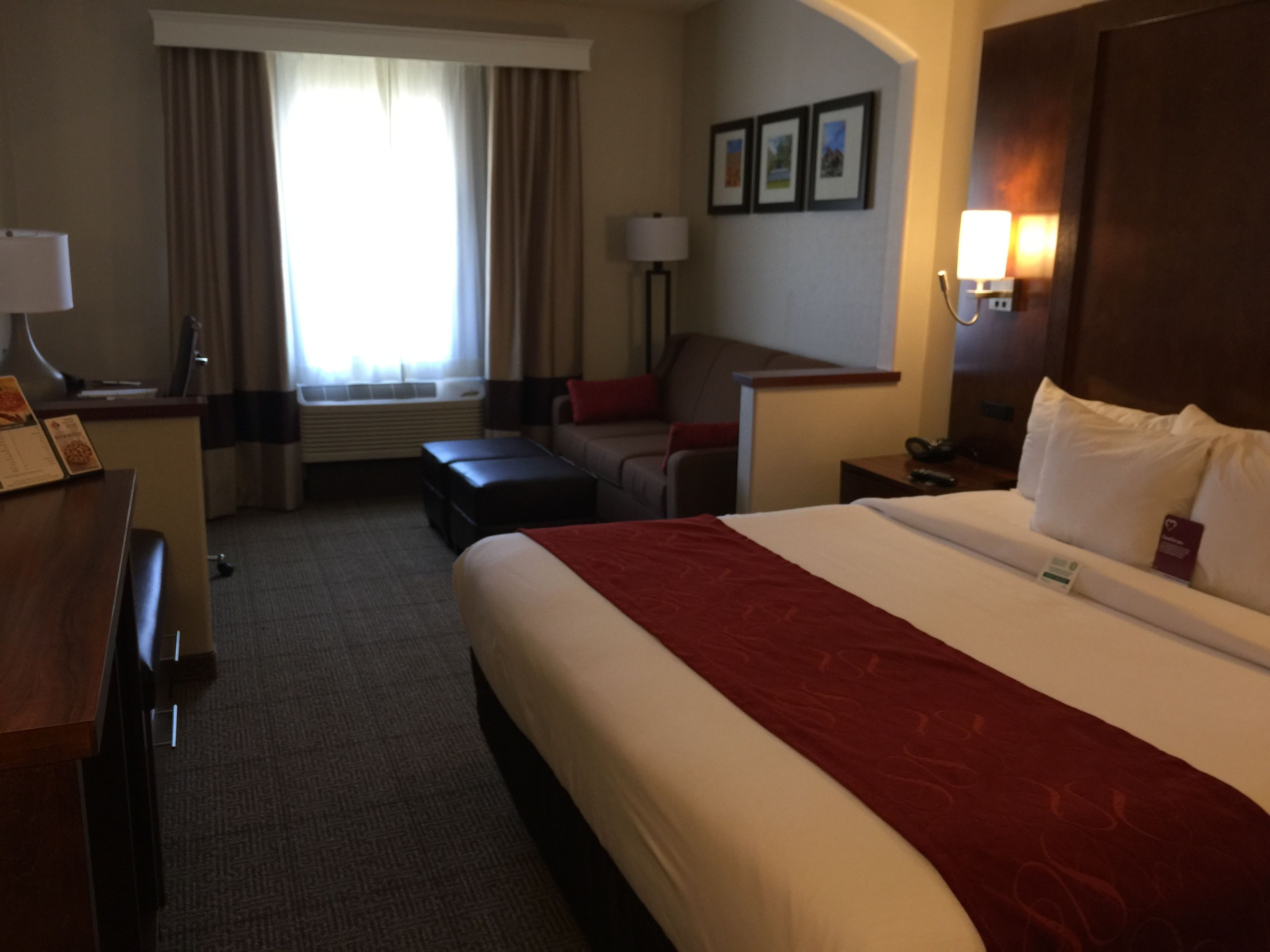 A hotel room with a large bed, a desk, a chair, a sofa, and a window with curtains.