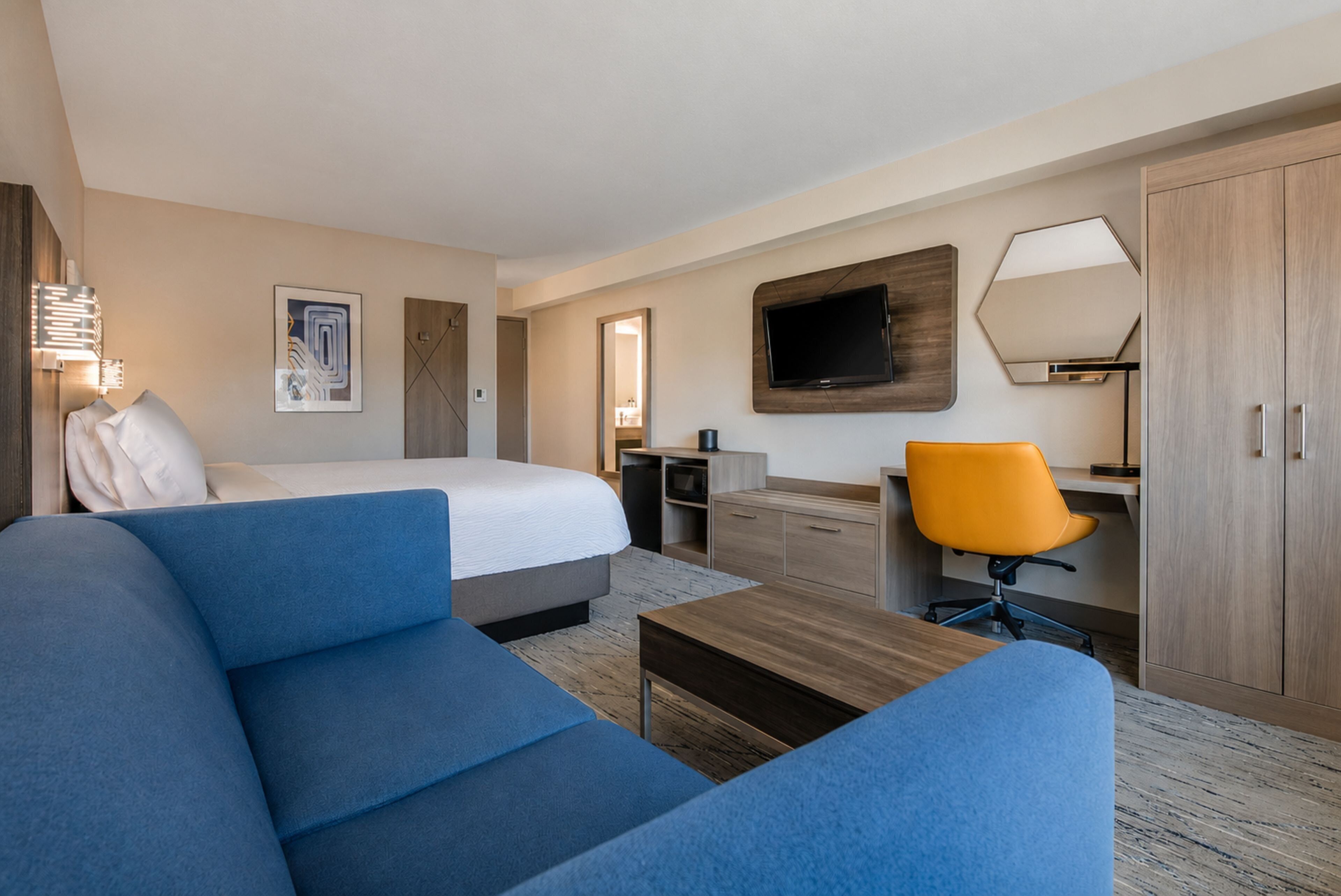 Ett hotellrum med en säng, en blå soffa, ett skrivbord med en stol, en tv och en garderob.