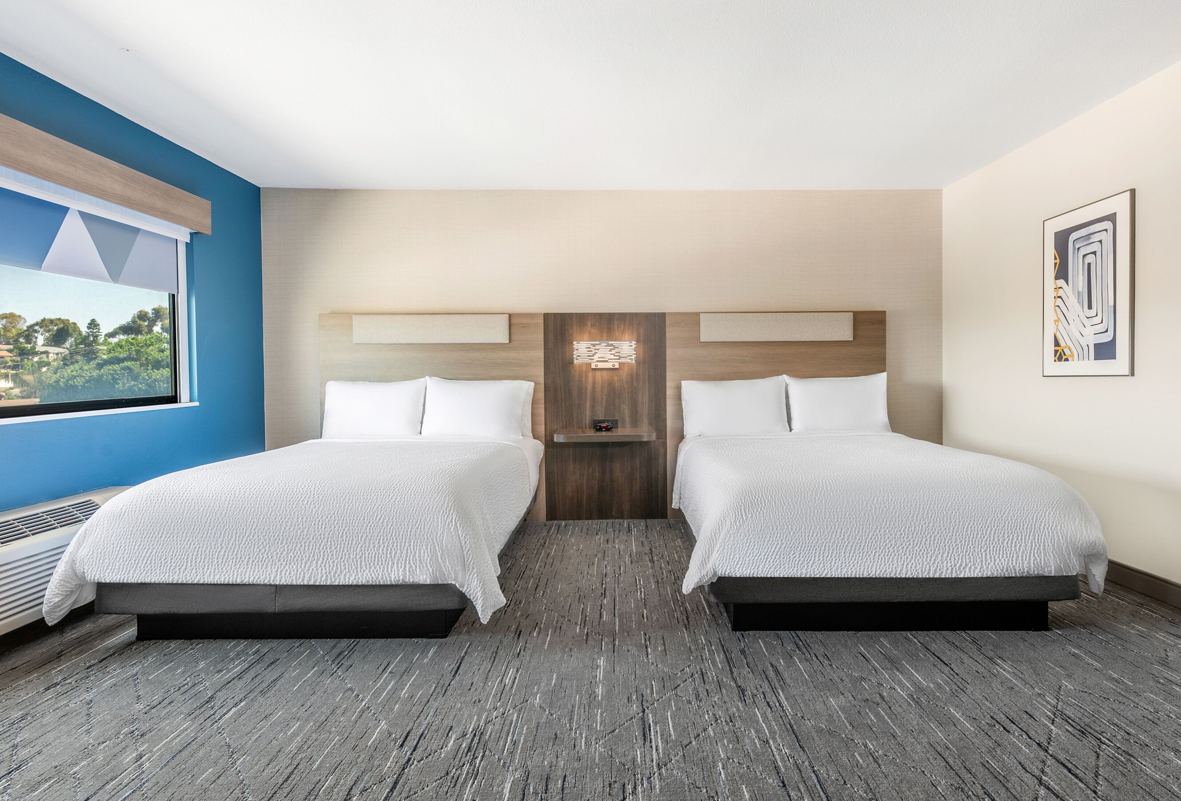 A hotel room with two beds, a large window, and a view of the outdoors.